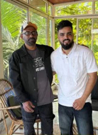 Two creative collaborators posing together outdoors, one in a white shirt.