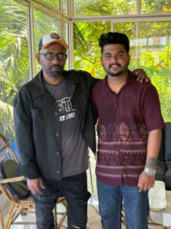 Two creative collaborators posing together outdoors, one in a maroon shirt.