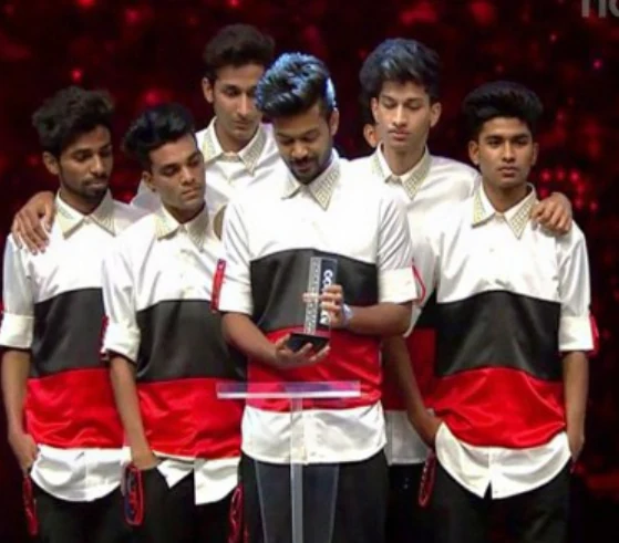 Dance crew in red, white, and black outfits gathered around an award on stage.
