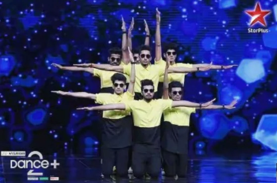 Dance crew in green performing a group acrobatic lift on stage.