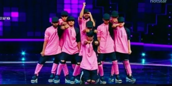 Crew in pink jackets performing under purple and blue stage lights.