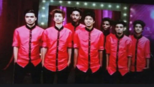 Dance crew posing in matching red jackets on a television stage.