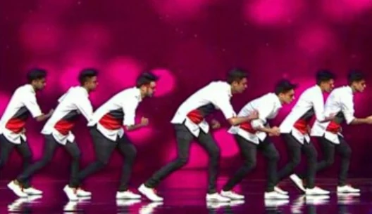 Dancers in red, white, and black outfits moving in formation under pink lights.
