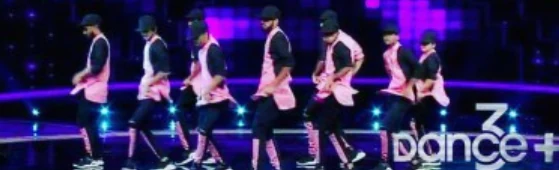Dancers in white shirts and dark trousers lined up during a stage routine.